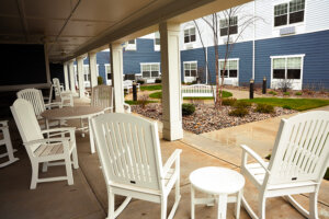 Photo of a patio with white rocking chairs and white side tables outside of North Bend Senior Living apartments