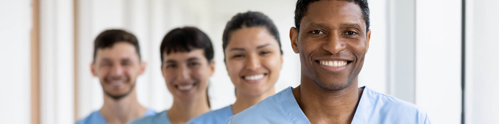 Four senior living facility employees wearing blue scrubs and smiling