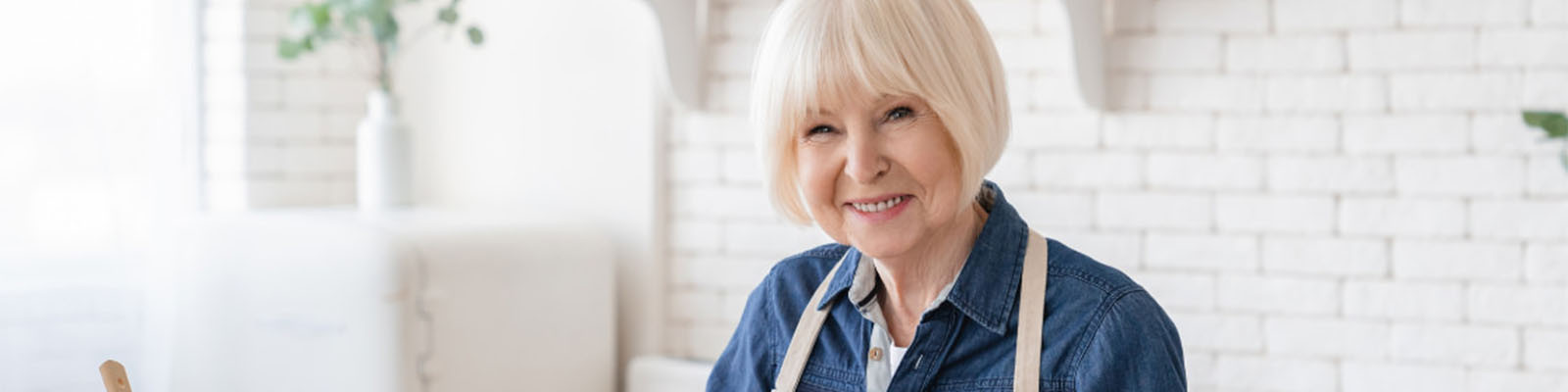 A senior woman smiling while standing in the kitchen wearing an apron