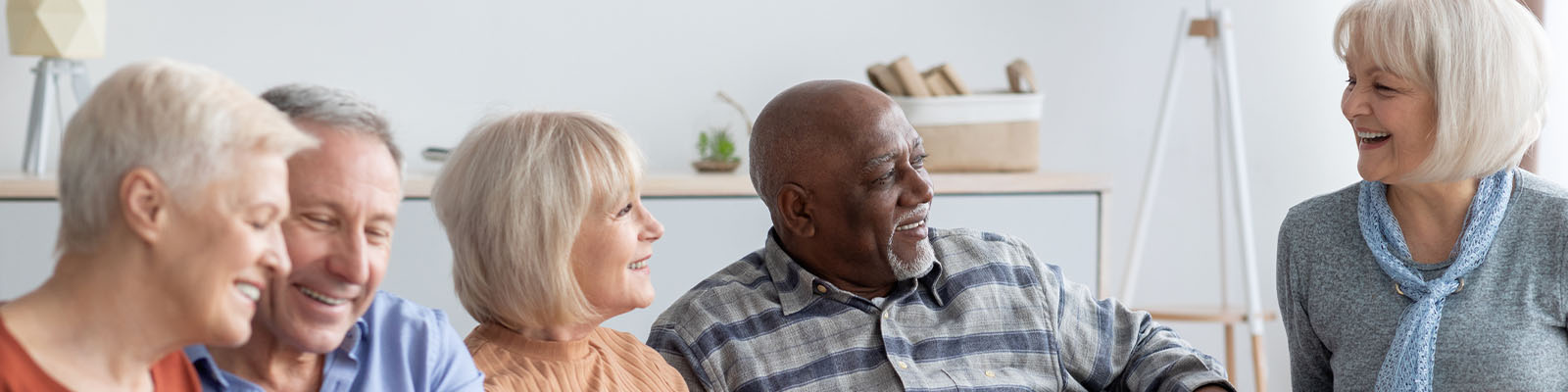 Senior men and women talking and sitting together in a community room at a senior living facility